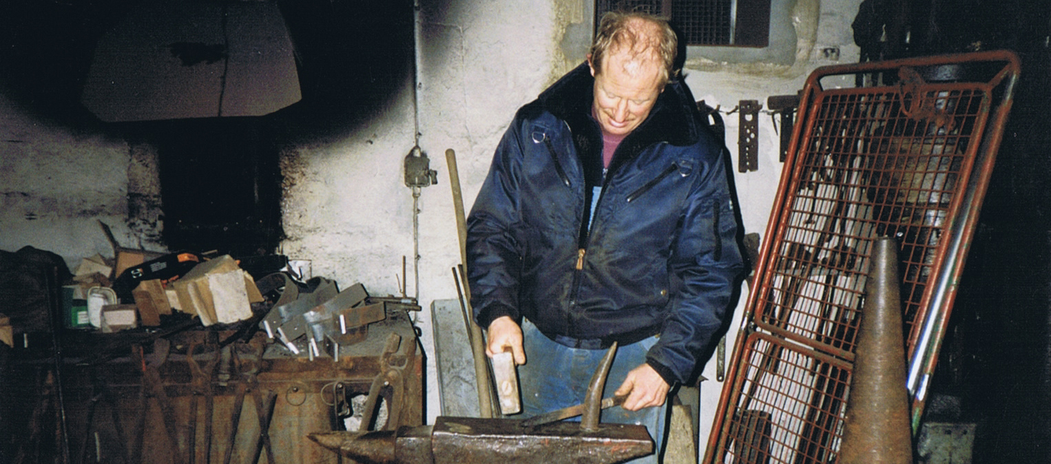 Ein Mitarbeiter bearbeitet ein Stück Stahl mit Hammer und Amboss